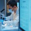 A molecular biologist working with a microscope in a modern scientific Laboratory, we see a computer screen in the foreground.CREDIT_iStock-1390303303