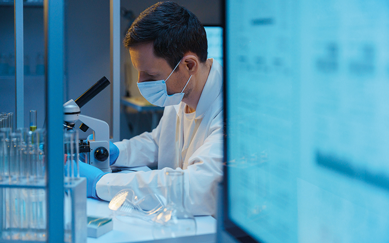 A molecular biologist working with a microscope in a modern scientific Laboratory, we see a computer screen in the foreground- CREDIT - istock-1390303303